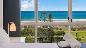 A hotel room with a large window offering a view of a beach and a clear sky. - Kirra Surf Apartments (Coolangatta)