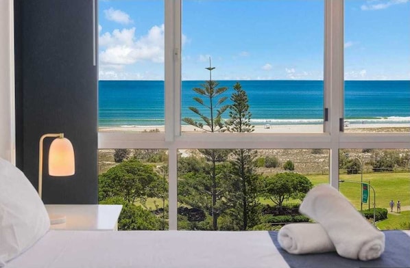 A hotel room with a large window offering a view of a beach and a clear sky. - Kirra Surf Apartments (Coolangatta)