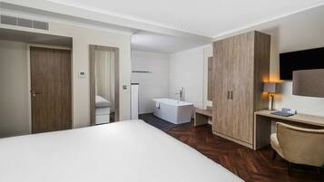 Una habitación de hotel moderna con una cama grande, un armario de madera, un escritorio con silla, un televisor de pantalla plana y un baño separado con bañera.