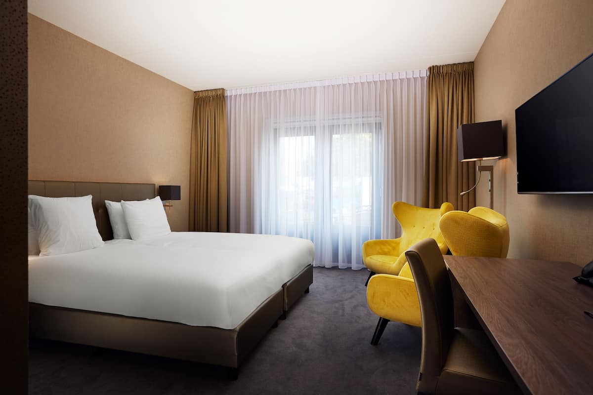 A hotel room with a large bed, a desk, a chair, and a TV.