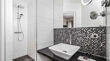 Un baño moderno con cabina de ducha de vidrio, un lavabo blanco y un salpicadero de azulejos.