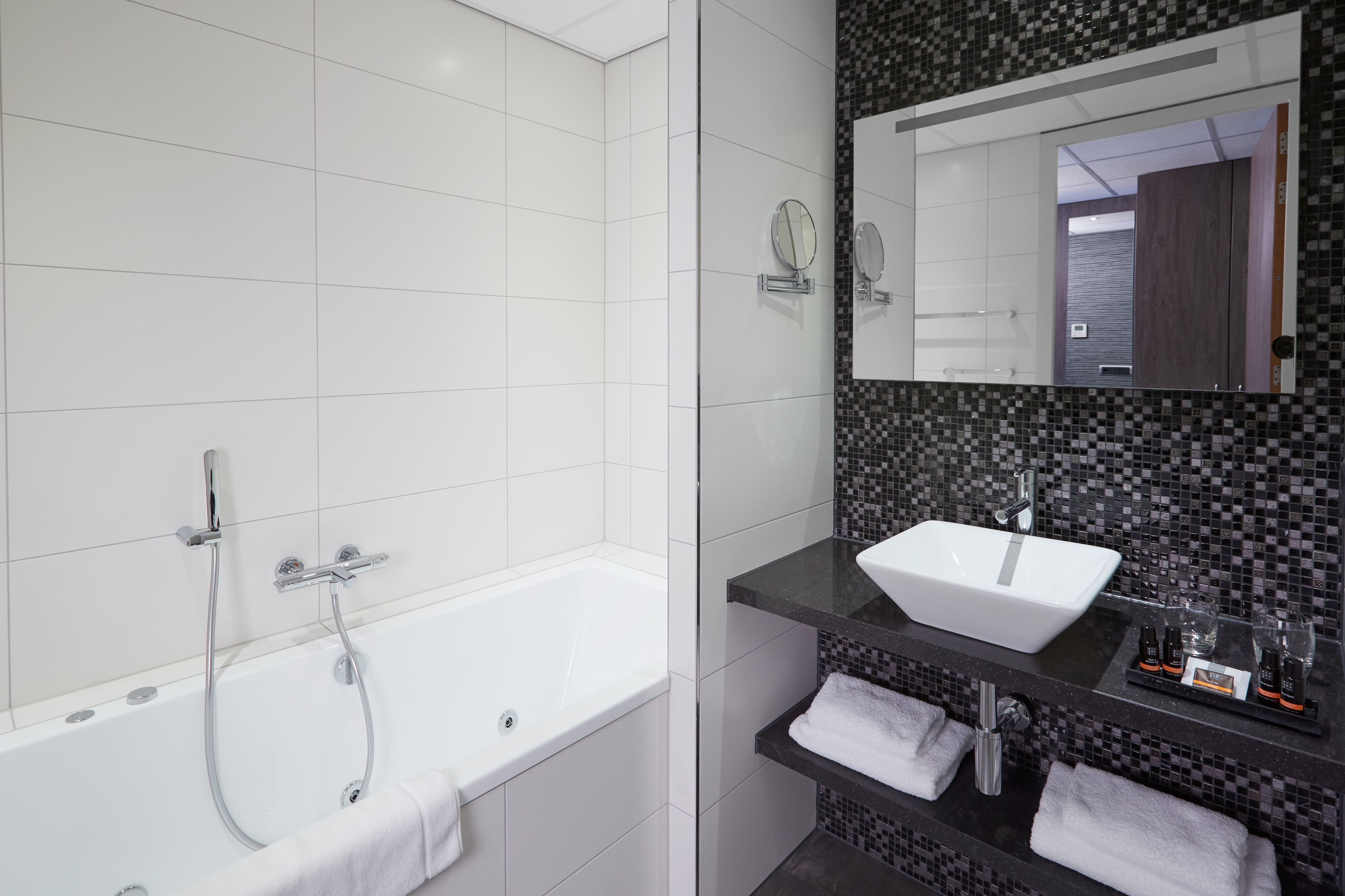 Une salle de bain moderne avec une baignoire blanche, un pare-feu noir en carreaux et un grand miroir au-dessus du lavabo.
