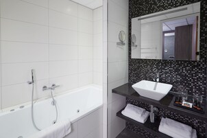 Une salle de bain moderne avec une baignoire blanche, un pare-feu noir en carreaux et un grand miroir au-dessus du lavabo.