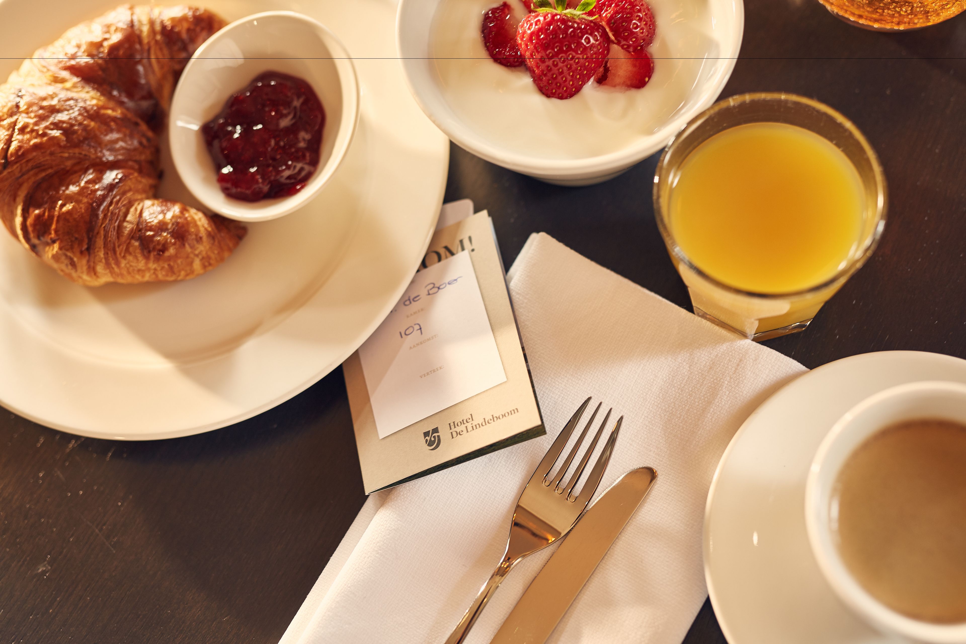 Ein Frühstückstisch mit Croissants, Erdbeeren, Marmelade, einem Glas Orangensaft und einer Speisekarte.