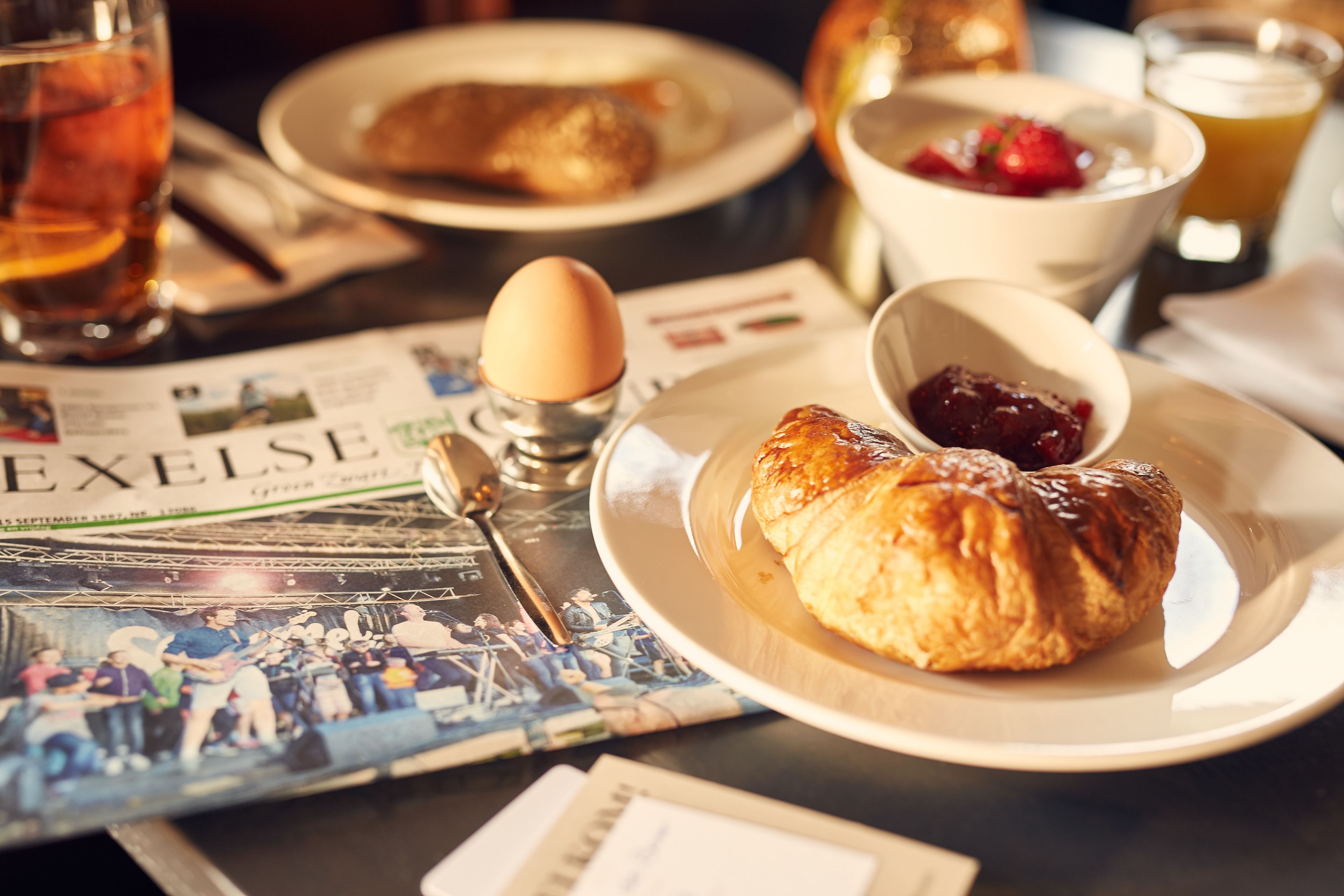 A breakfast setting with croissants, a cup of tea, and a newspaper.