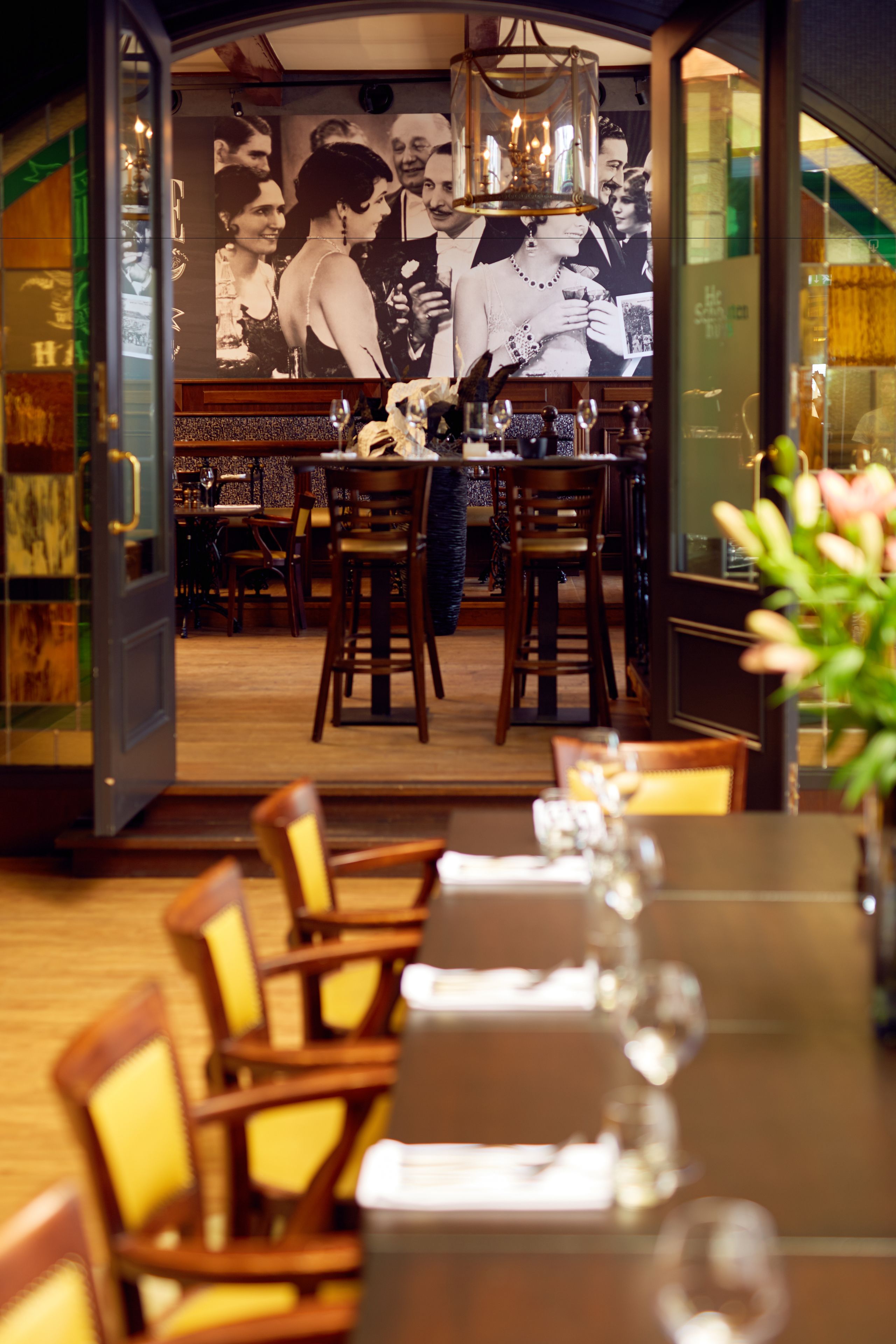 Un restaurant avec des chaises et des tables en bois, un lustre et une grande photographie en noir et blanc accrochée au mur.