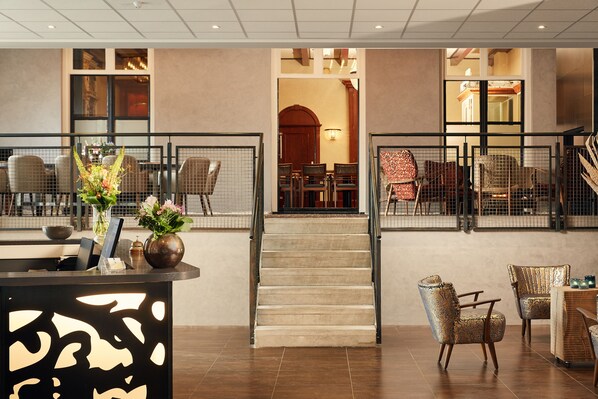 Un vestíbulo de hotel con mostrador de recepción, zona de estar y una escalera que lleva a otro nivel.