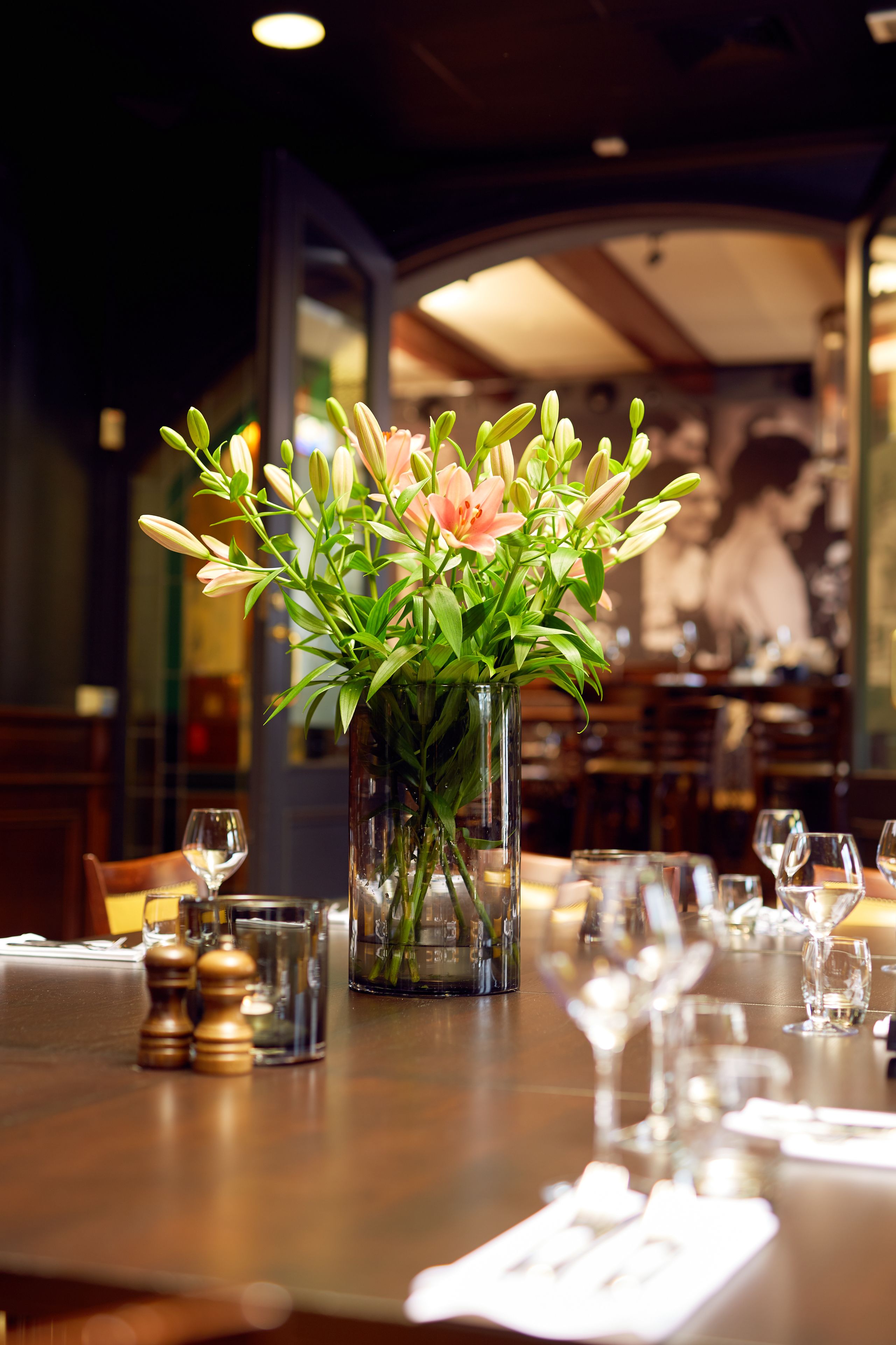 A dining table set with a vase of flowers, glasses, and cutlery.