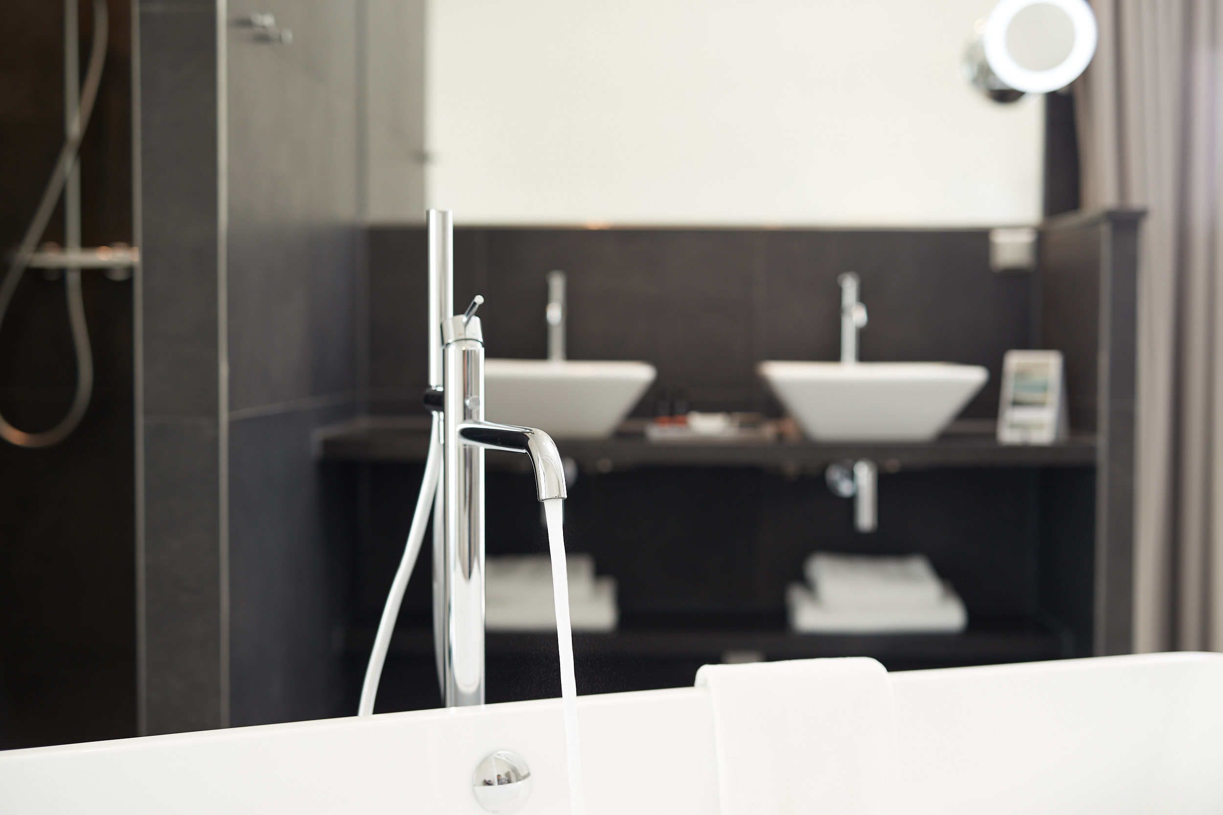 Un baño moderno con grifo de cromo, lavamanos blanco y espejo sobre el lavamanos.