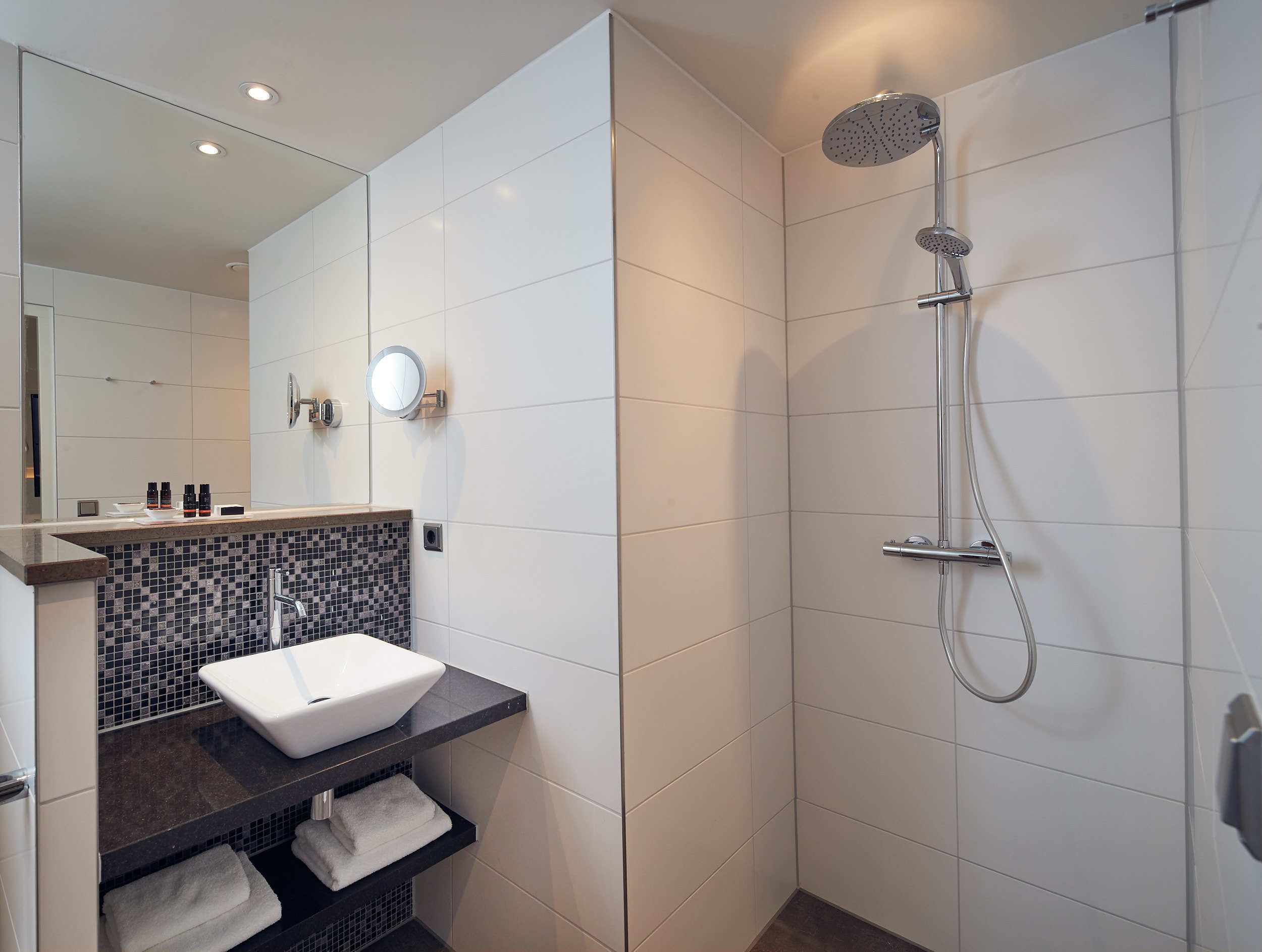 A modern bathroom with a white sink, a shower with a handheld showerhead, and a tiled backsplash.