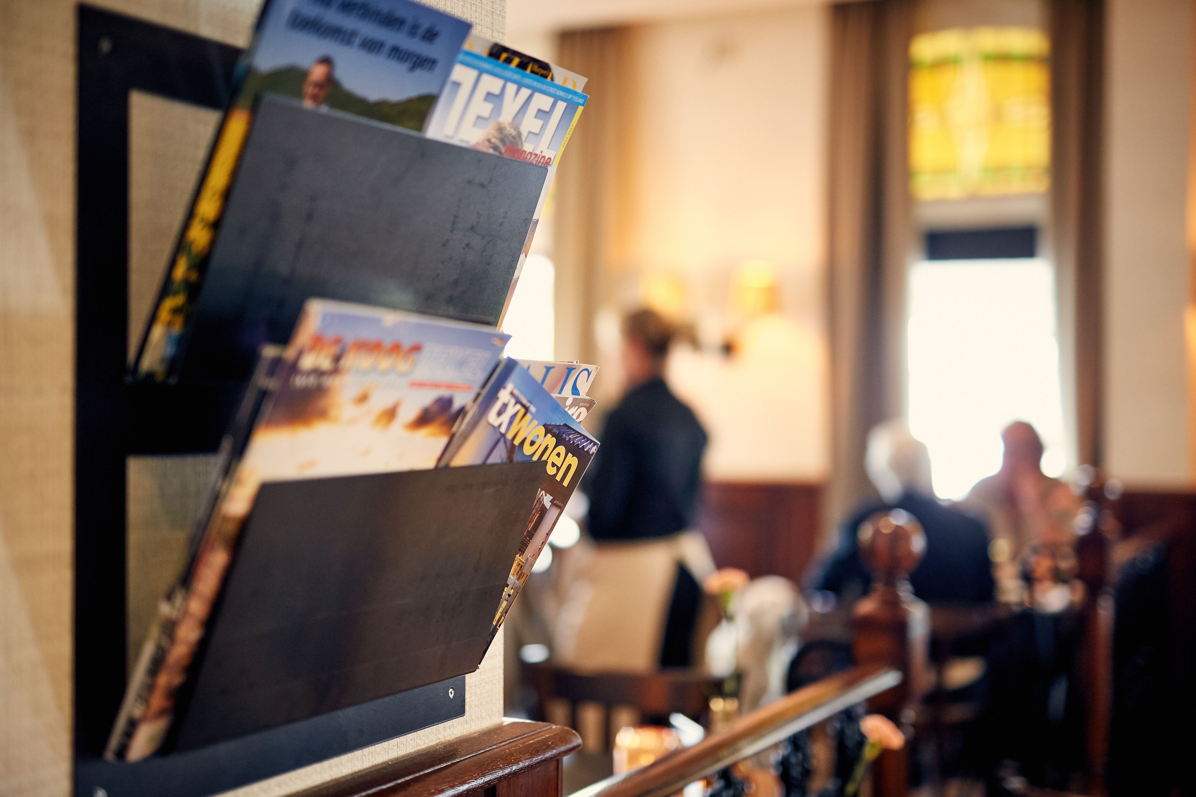 A magazine rack with various publications, a wooden counter, and a blurred background of a dining area.