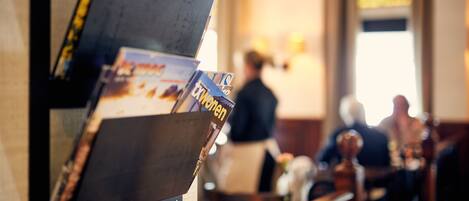 A magazine rack with various publications, a wooden counter, and a blurred background of a dining area.