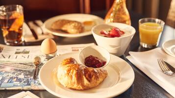 Un desayuno con croissants, un bol de compota de frutas, un vaso de jugo de naranja y un periódico.