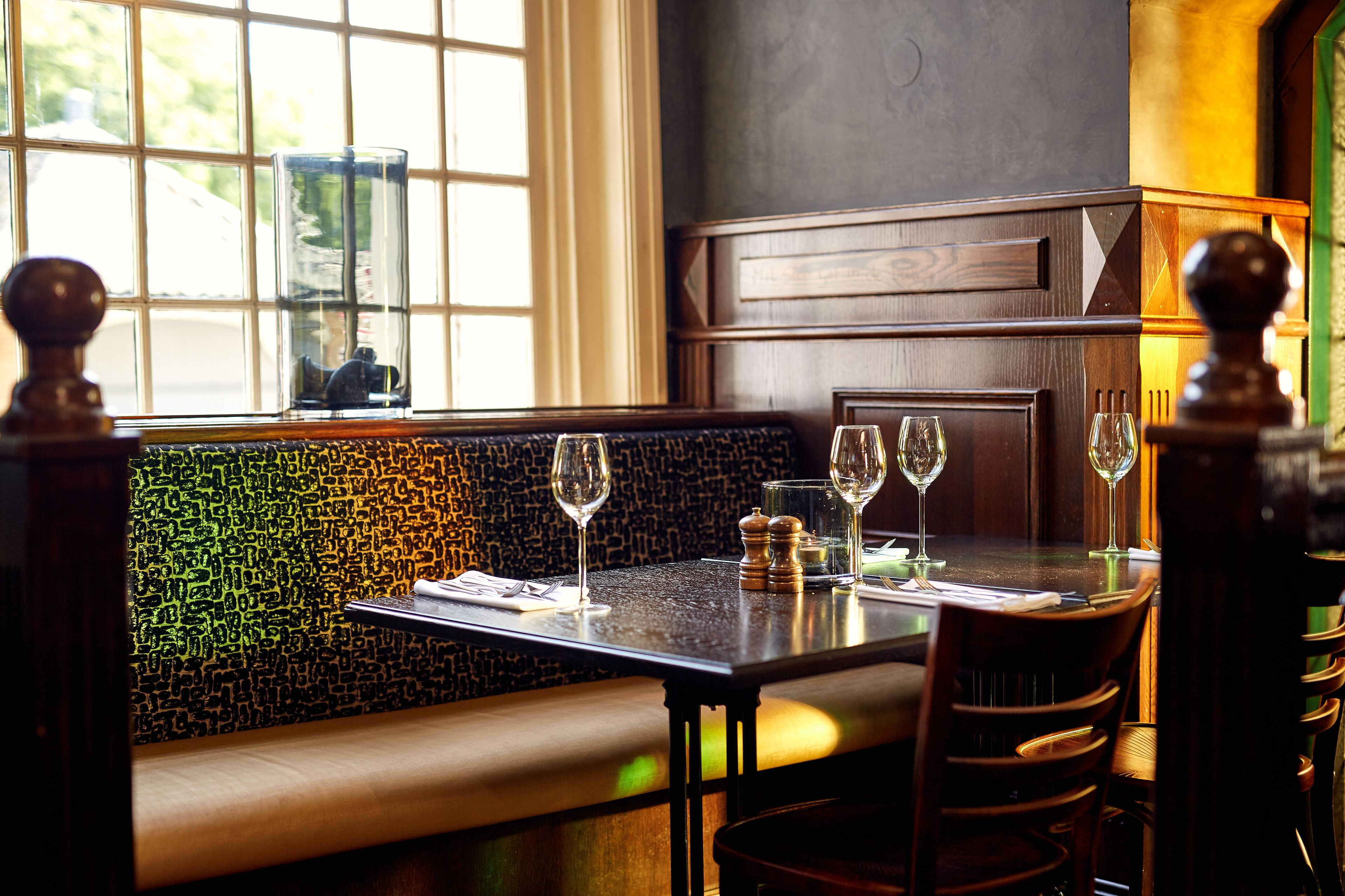 Interior de restaurante con zona de cabinas, una mesa con copas de vino y pared decorada.