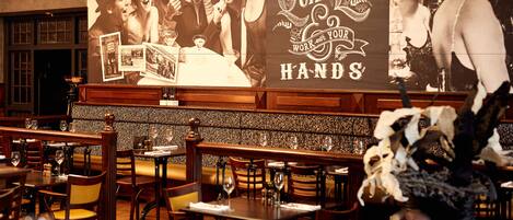 A restaurant interior with wooden tables and chairs, a brick wall, and a large poster advertising 'Live a Quiet Life'.