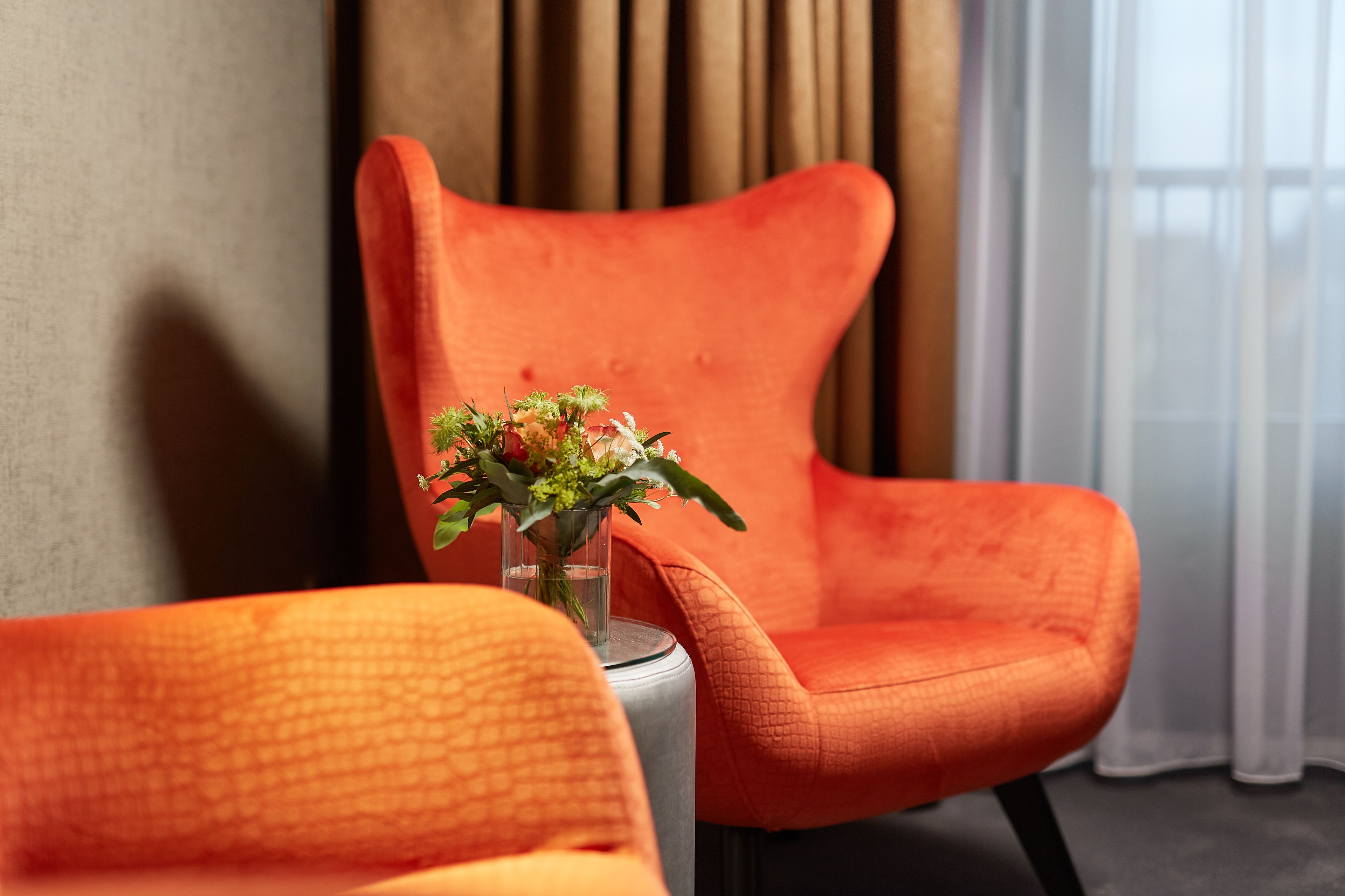Une pièce avec un fauteuil orange moderne et une petite table sur laquelle est posé un vase de fleurs.