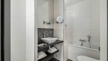 A modern bathroom with a white sink, a black shelf with towels, a mirror, and a bathtub.