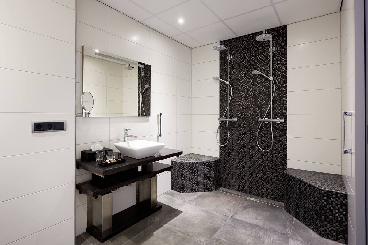 A modern bathroom with a white sink, dark countertop, and a shower with a mosaic tile wall.