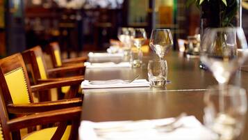 A dining table set with white napkins, cutlery, and wine glasses, with chairs upholstered in yellow.