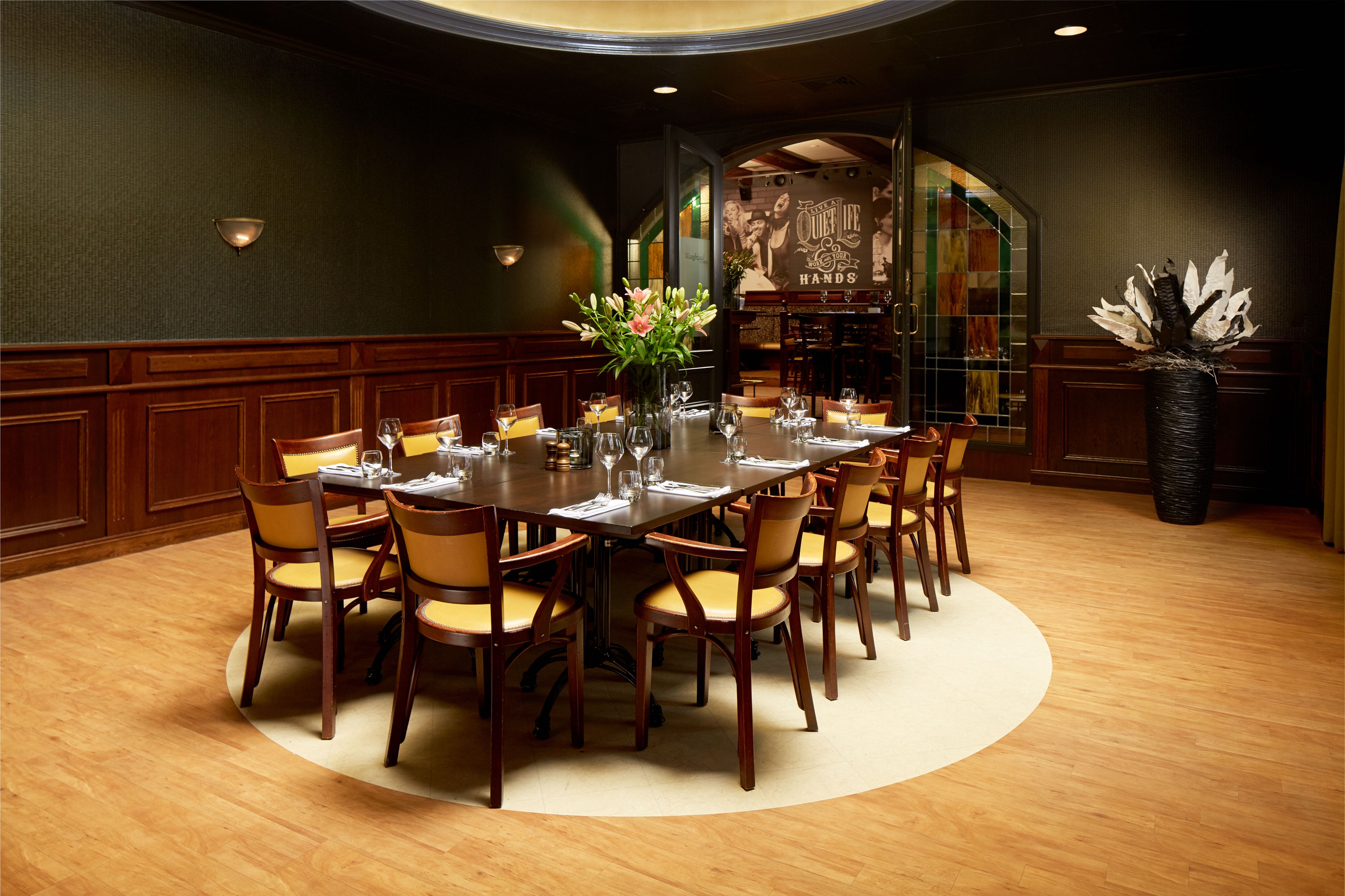 Uma sala de jantar formal com uma mesa redonda, várias cadeiras e um vaso de flores.