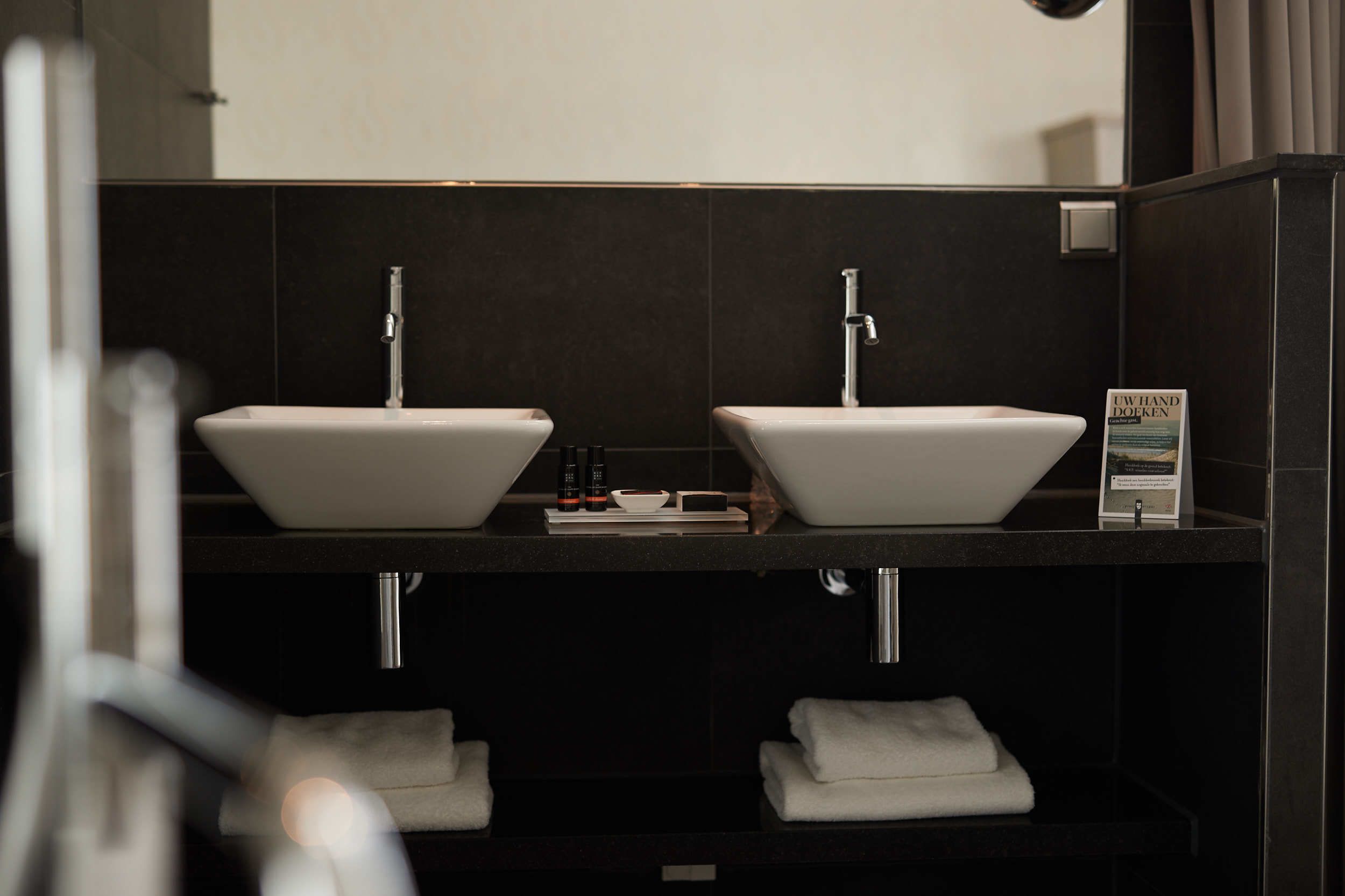 Uma casa de banho moderna com duas bacias brancas, um espelho e um porta-toalhas.
