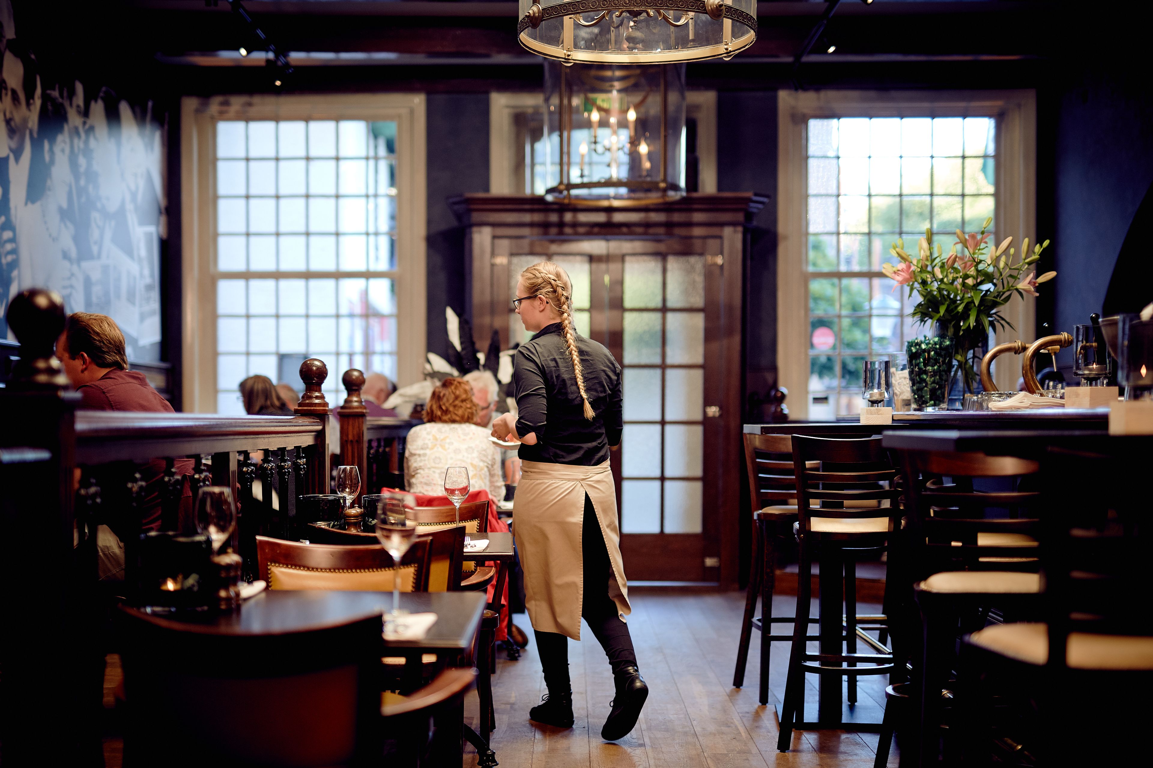 A restaurant interior with wooden tables, chairs, and a bar area.