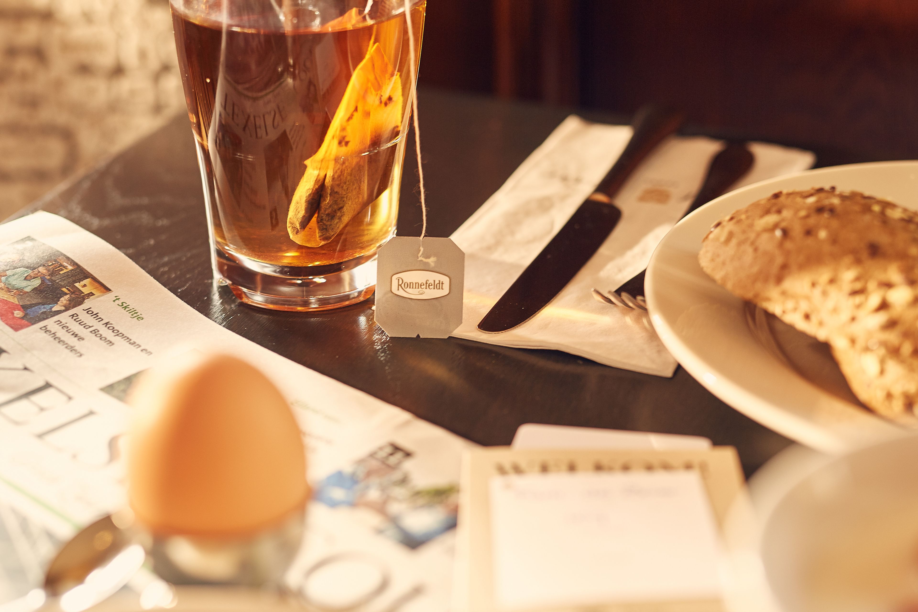 A table with a glass of tea, a teabag, a plate with a pastry, a spoon, and a calendar.