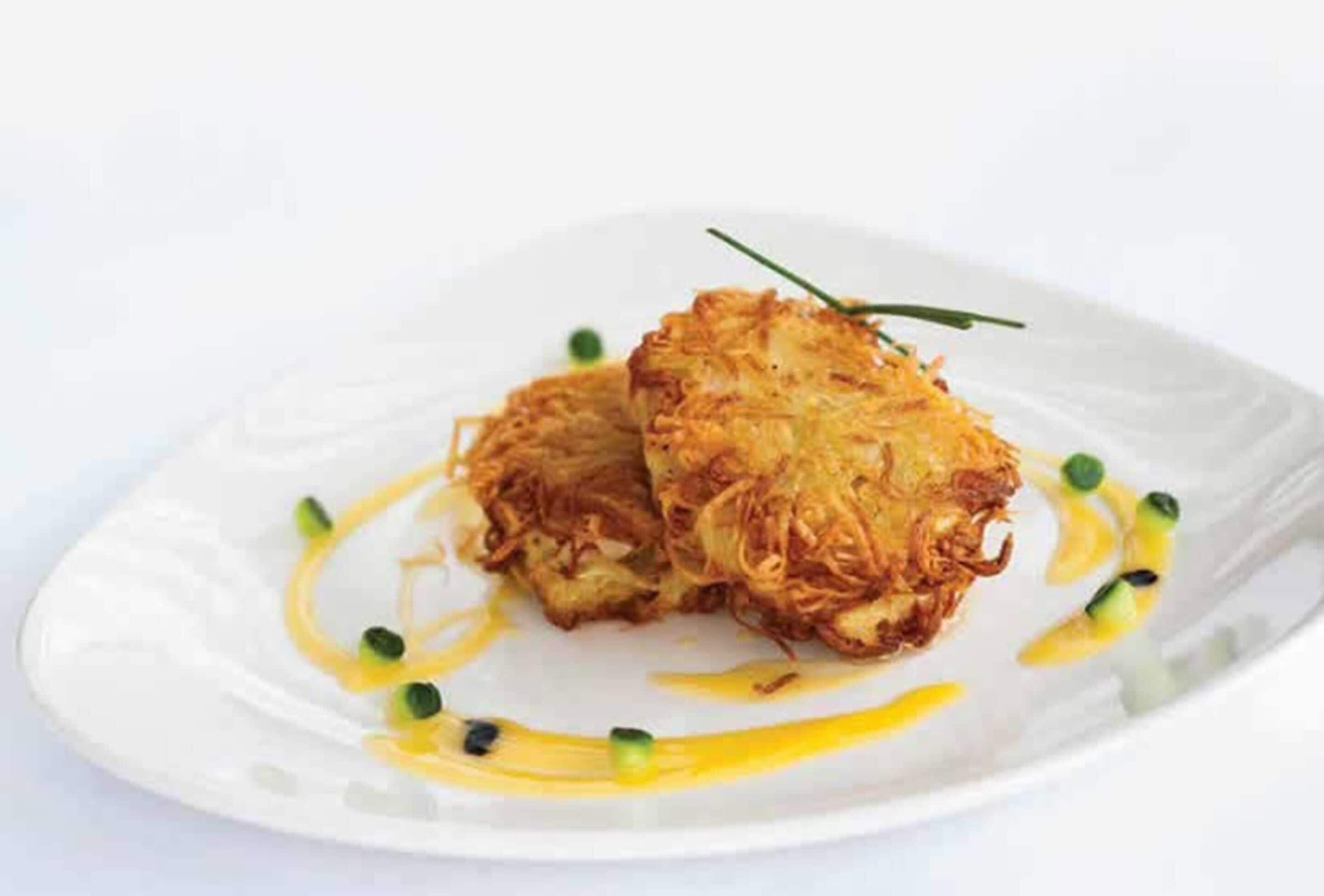 Two crispy, golden-brown pancakes on a white plate with a drizzle of sauce and green garnish.
