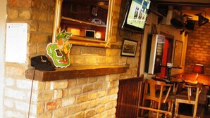 Un pub acogedor con chimenea de piedra, mobiliario de madera y un televisor en la pared.
