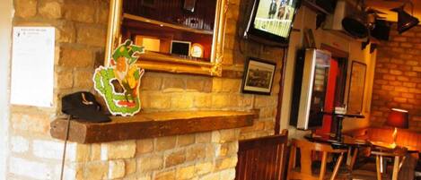 Un pub acogedor con chimenea de piedra, mobiliario de madera y un televisor en la pared.