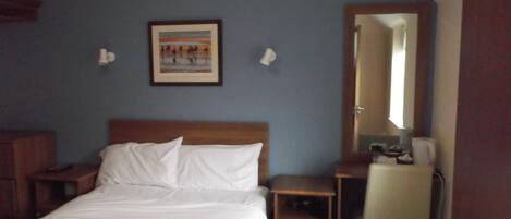Habitación de hotel con cama, escritorio, silla, mesita de noche y espejo.