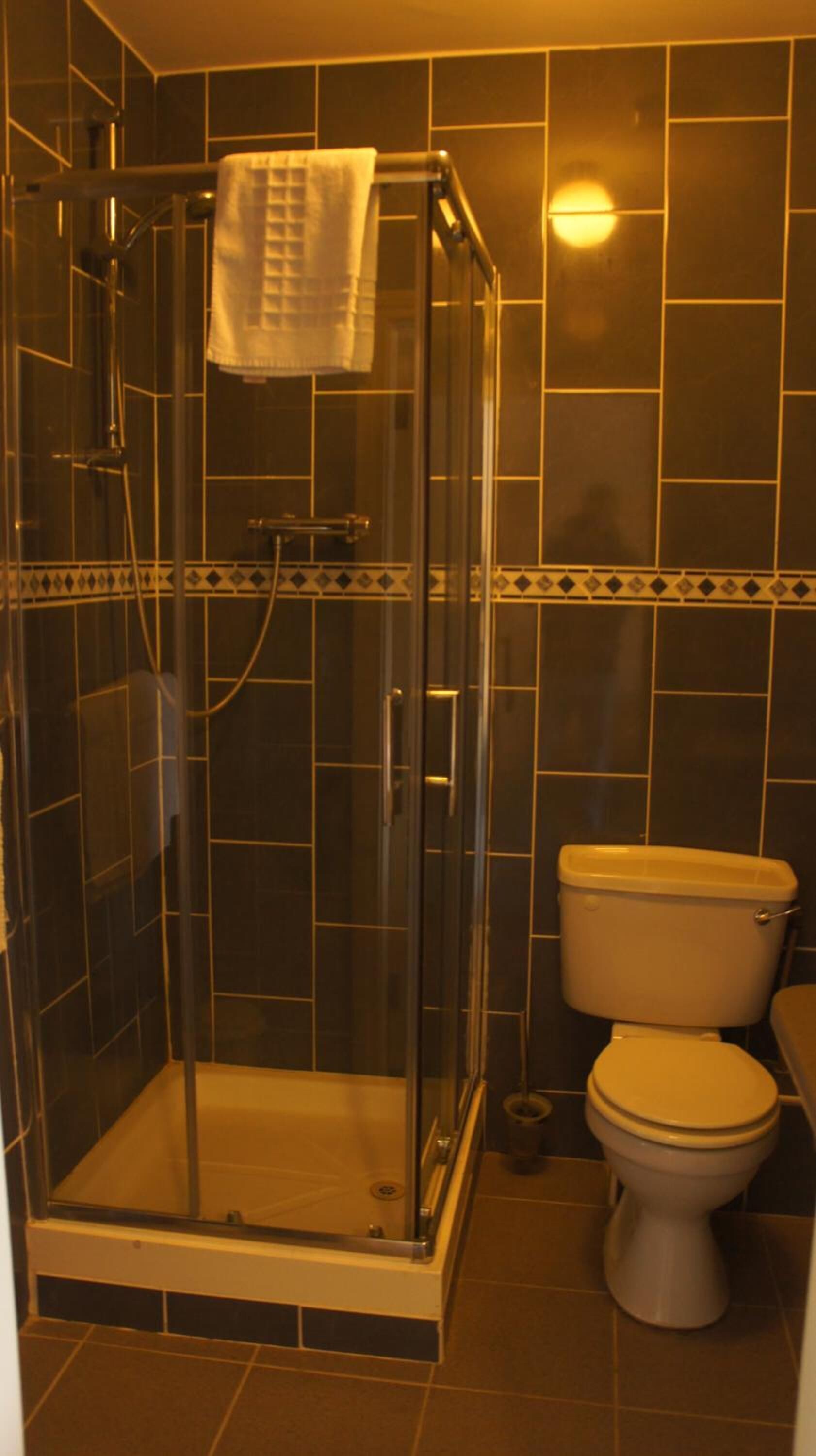 Un vestuario con cabina de ducha de vidrio, una toalla colgada en la puerta, un inodoro y paredes de azulejos.