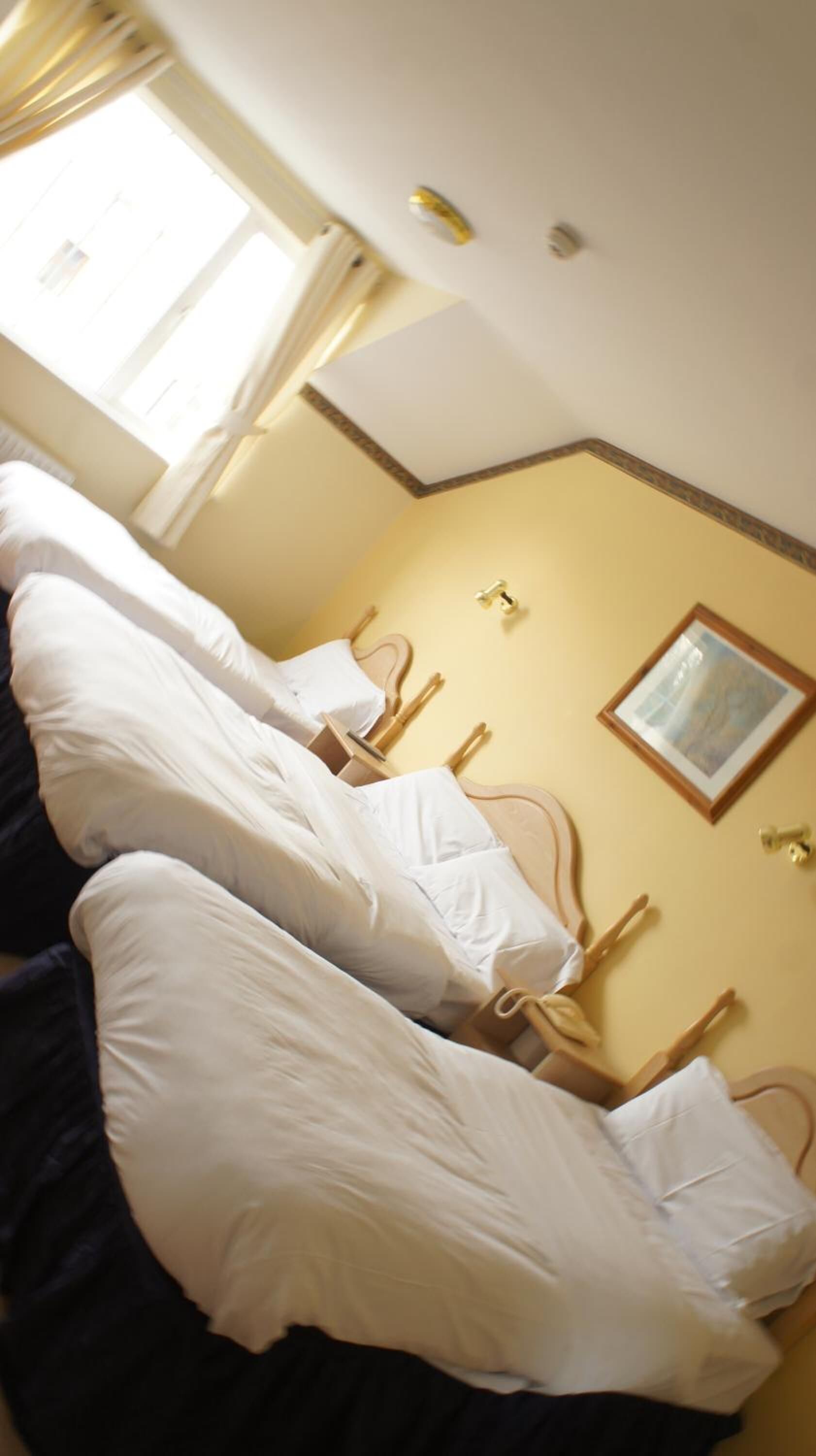 Ein Hotelzimmer mit Bett, Nachttisch, einem Wandbild und einem Fenster mit Vorhängen.