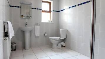 Ein Badezimmer mit weißen Fliesen, einem Waschbecken, einer Toilette und einem Fenster.