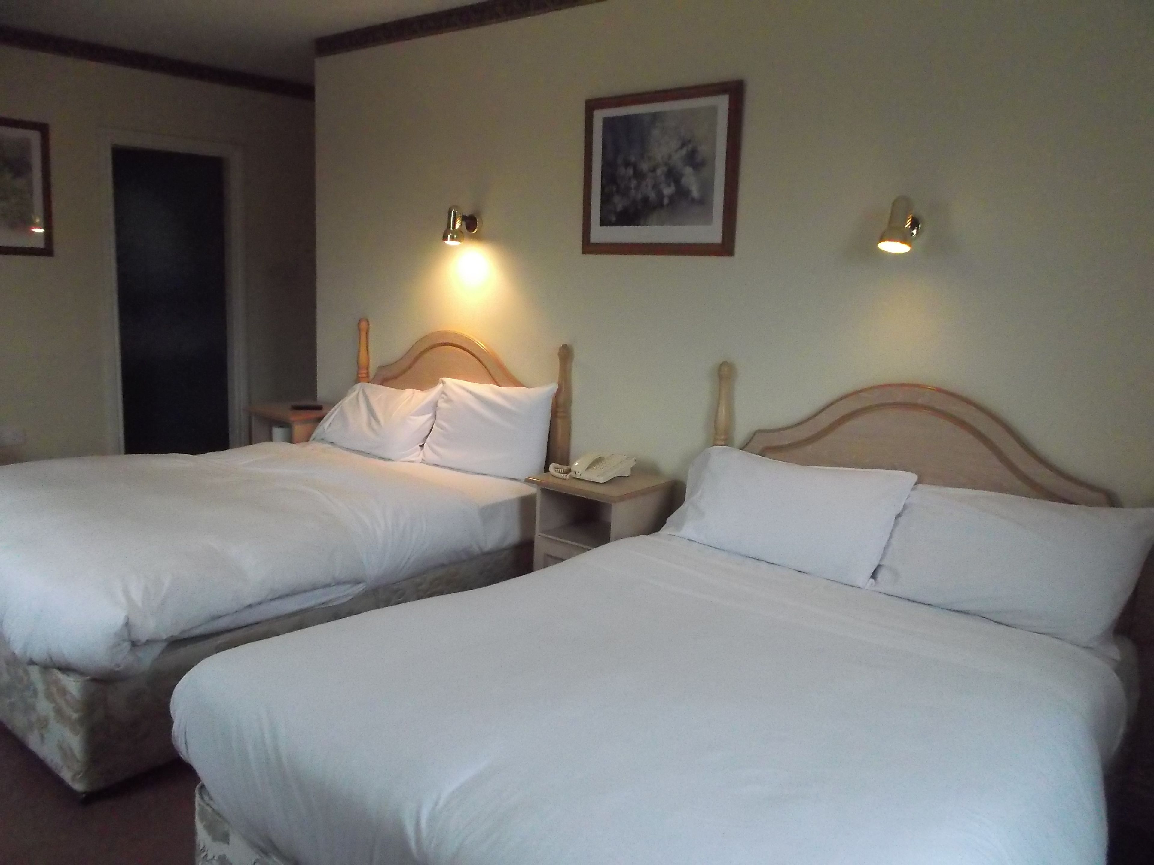 A hotel room with two single beds, a bedside table with a lamp, and a framed picture on the wall.