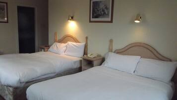 A hotel room with two single beds, a bedside table with a lamp, and a framed picture on the wall.