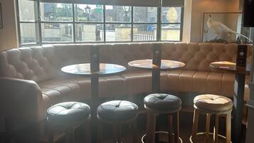 A cozy seating area with a leather couch and round tables, wooden stools, and a large window offering a view of the street.