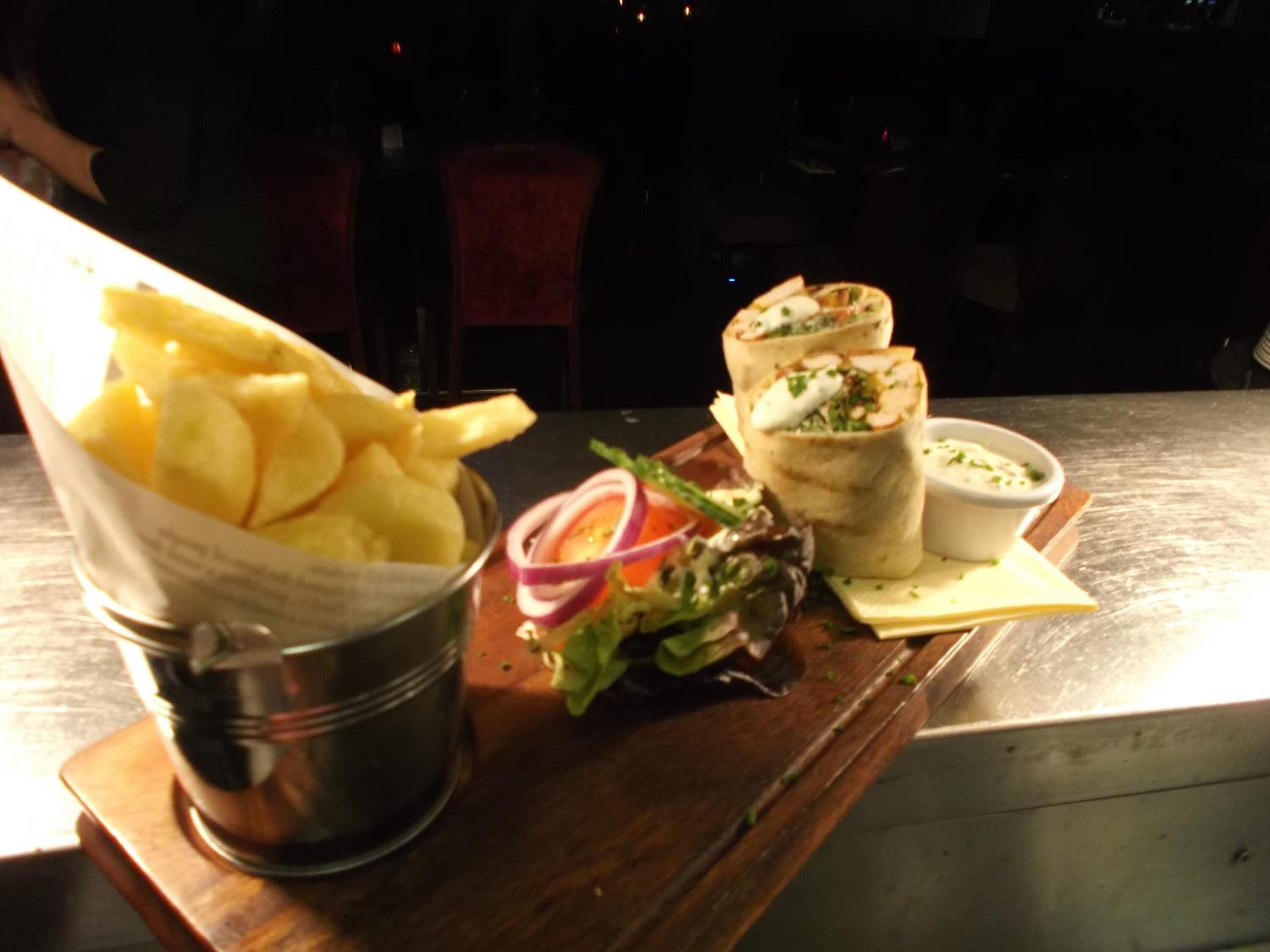 Un repas composé d’un wrap, d’une salade et d’un bol de frites, le tout servi sur une table en bois.