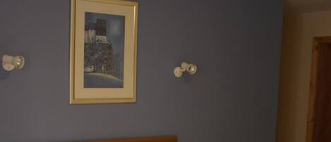 A neatly made bed with white linens, a wooden headboard, and a dark blue skirt. There is a framed picture on the wall above the bed.