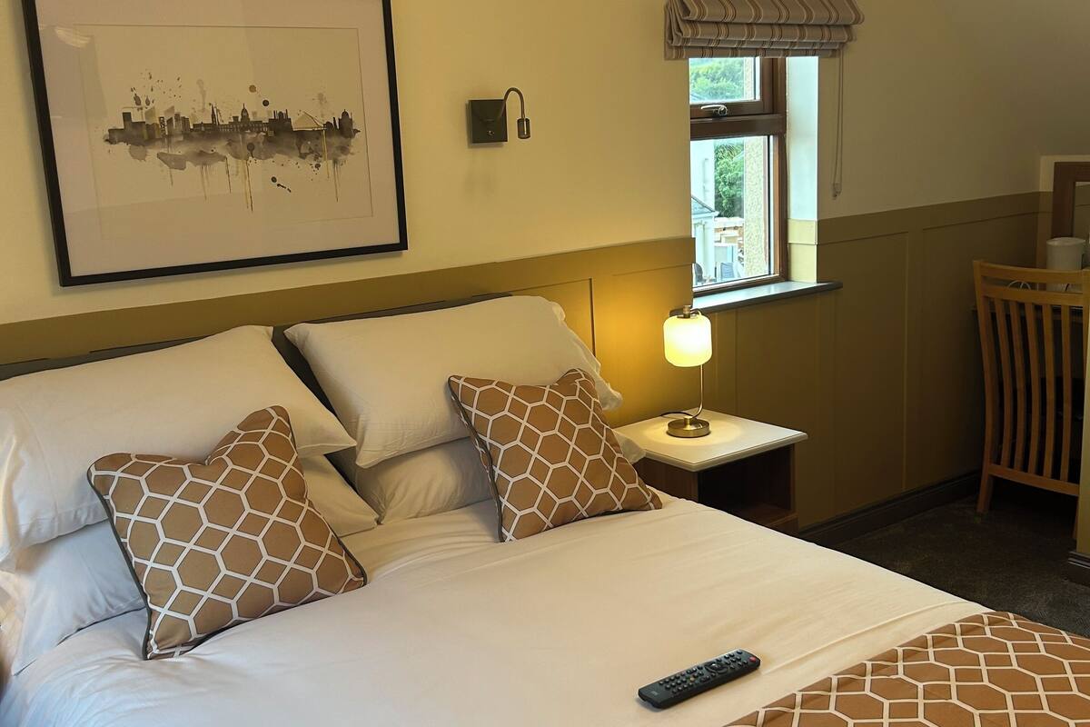 A hotel room with a bed, a nightstand, a lamp, a chair, a window with curtains, and a framed picture on the wall.