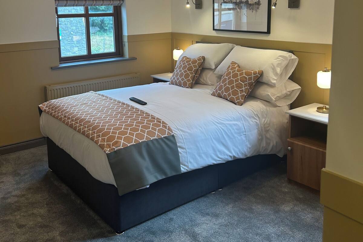 A neatly arranged bedroom with a large bed, bedside lamps, a window with curtains, and a framed picture on the wall.