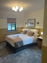 Un dormitorio ordenado con una cama grande, lámparas de noche, un ventanal con cortinas y un cuadro en la pared.