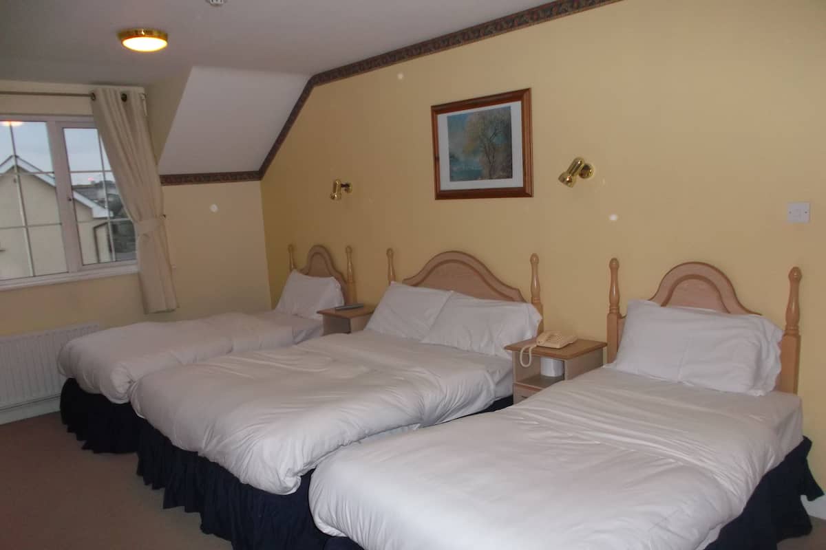 A hotel room with two single beds, a small bedside table with a telephone, and a window with curtains.