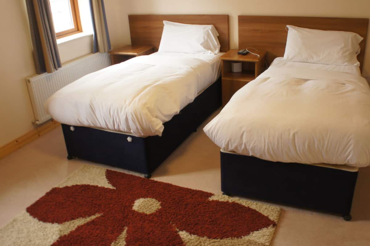 Two single beds with wooden headboards in a room with a radiator and a window with curtains.