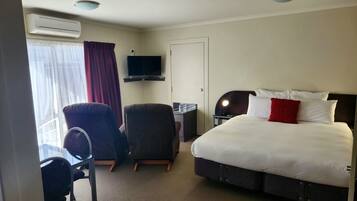 Una habitación de hotel con una cama, dos sillas, un escritorio, un televisor y un equipo de aire acondicionado.