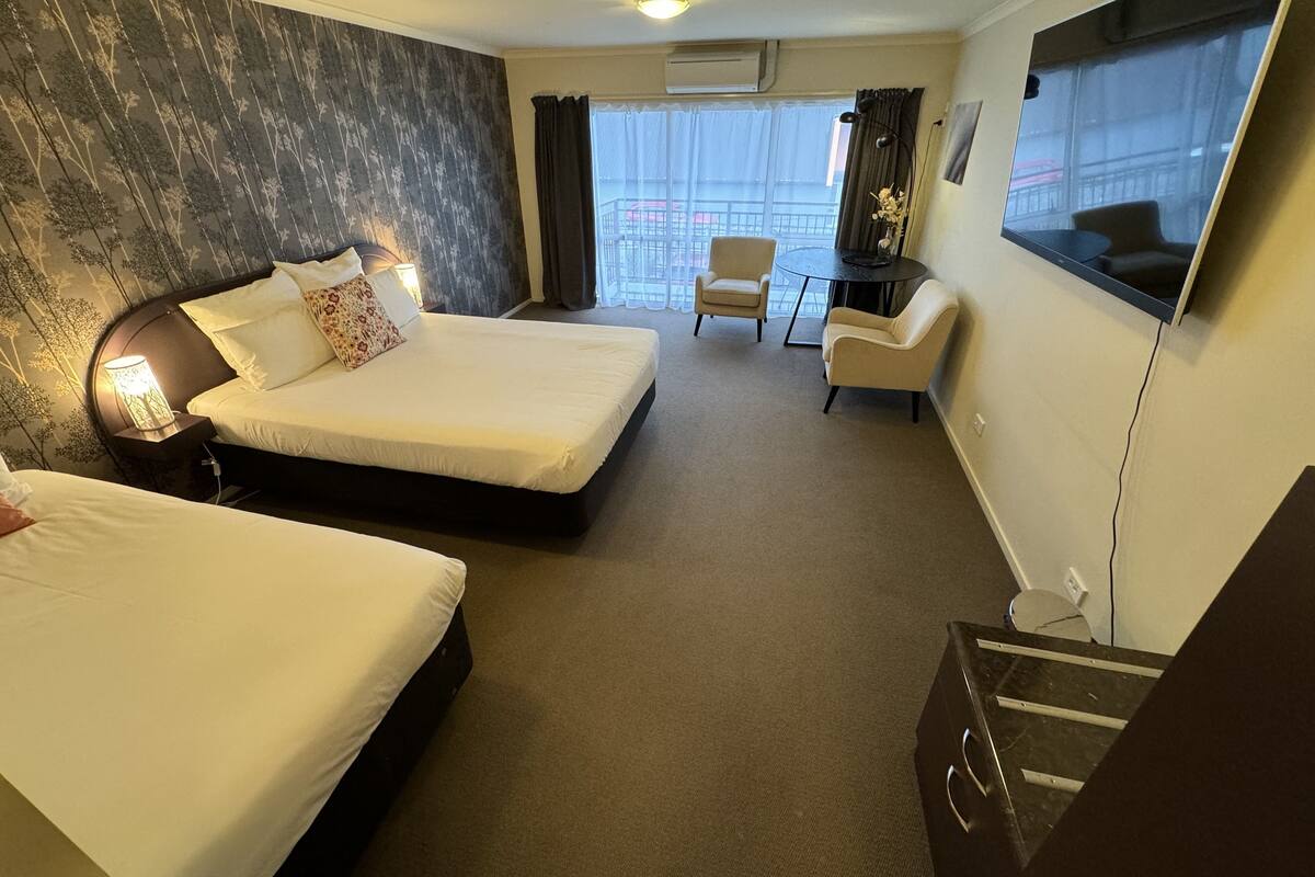 A hotel room with two beds, a desk, a chair, and a large window with a view.