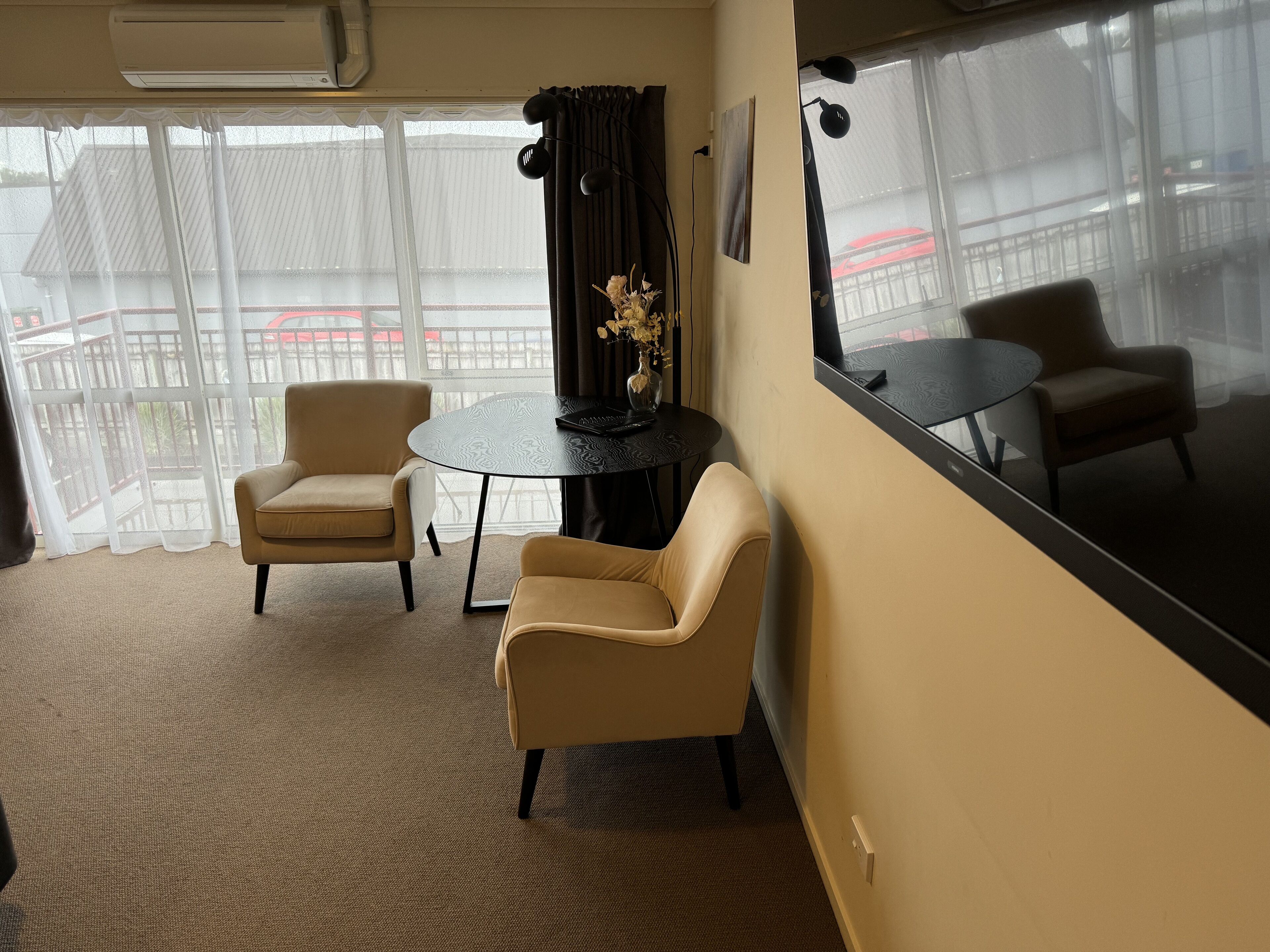 A room with two beige armchairs, a small round table, and a large mirror on the wall.