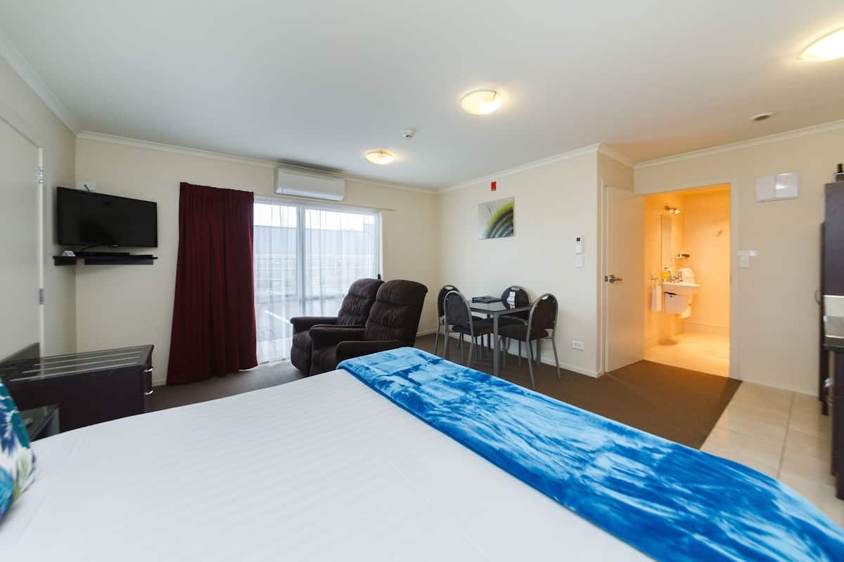 A hotel room with a bed, a TV, a desk with chairs, and a bathroom.