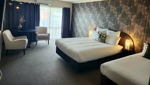 A hotel room with a large bed, a smaller bed, a desk with a chair, and a window with curtains.