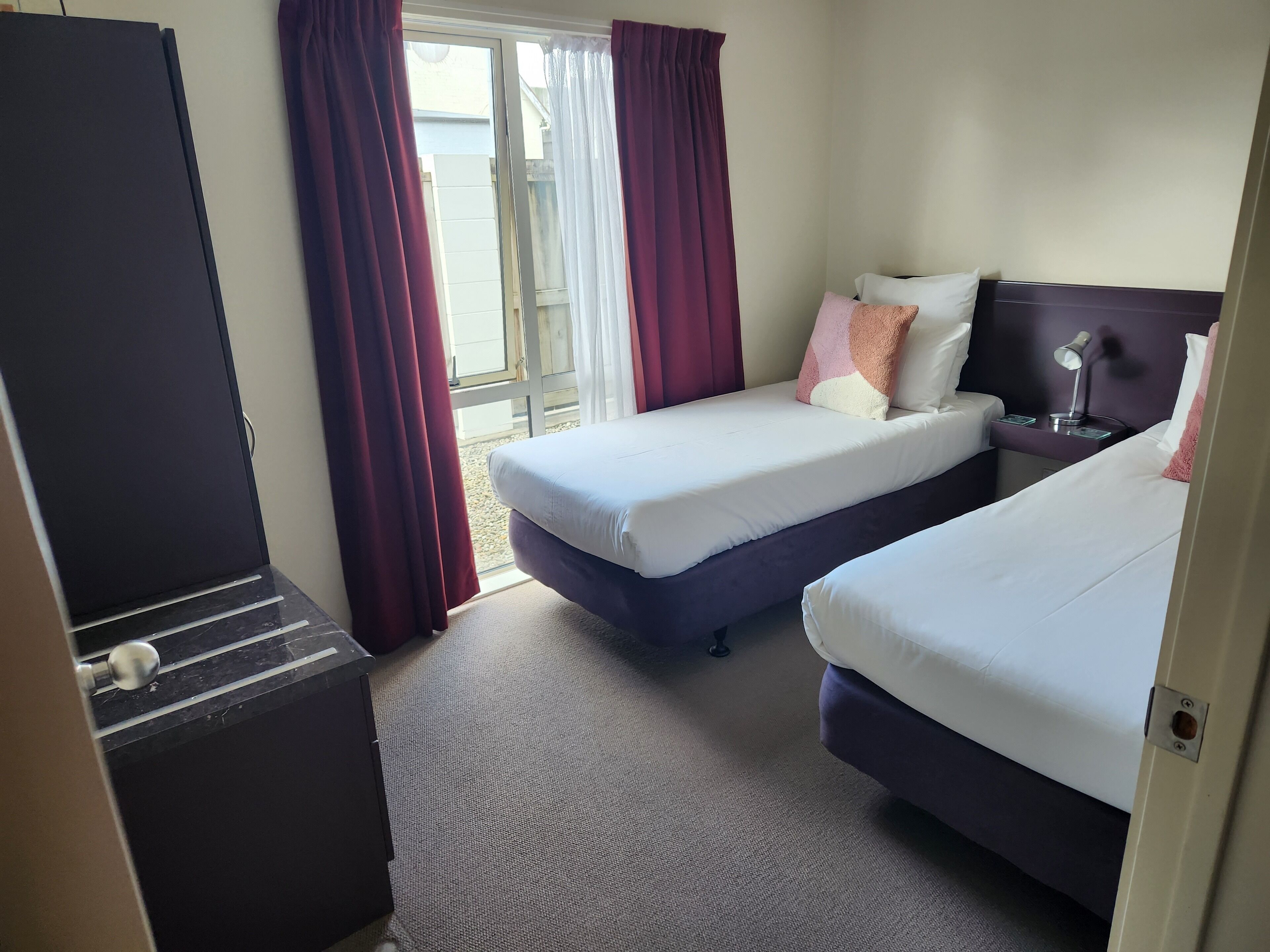 Een hotelkamer met twee bedden, een bureau, een stoel en een raam met gordijnen.